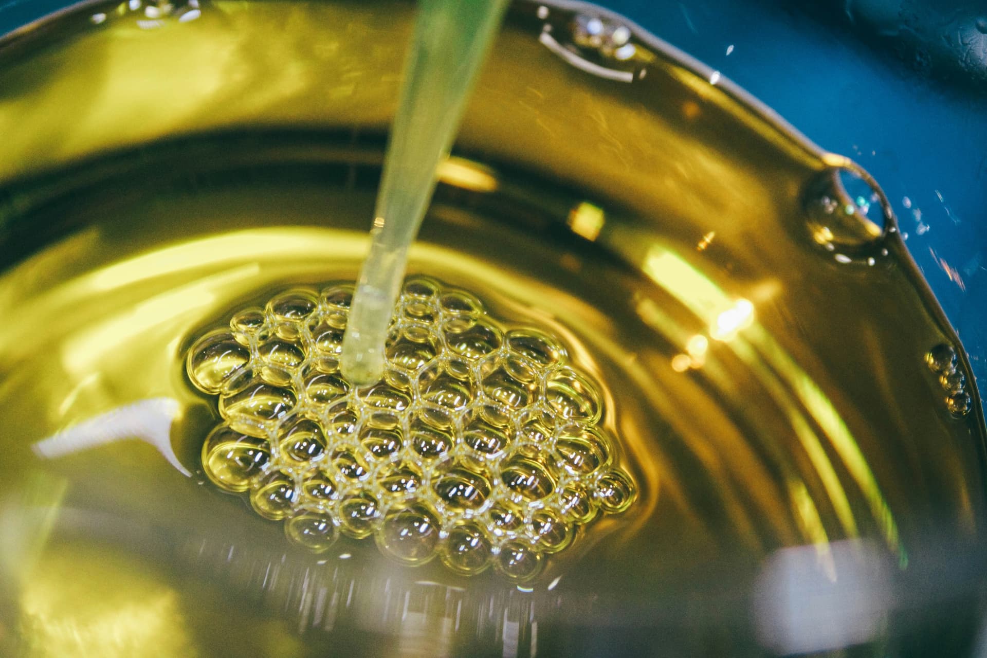 Golden edible oil pouring into a stainless vessel with bubbles