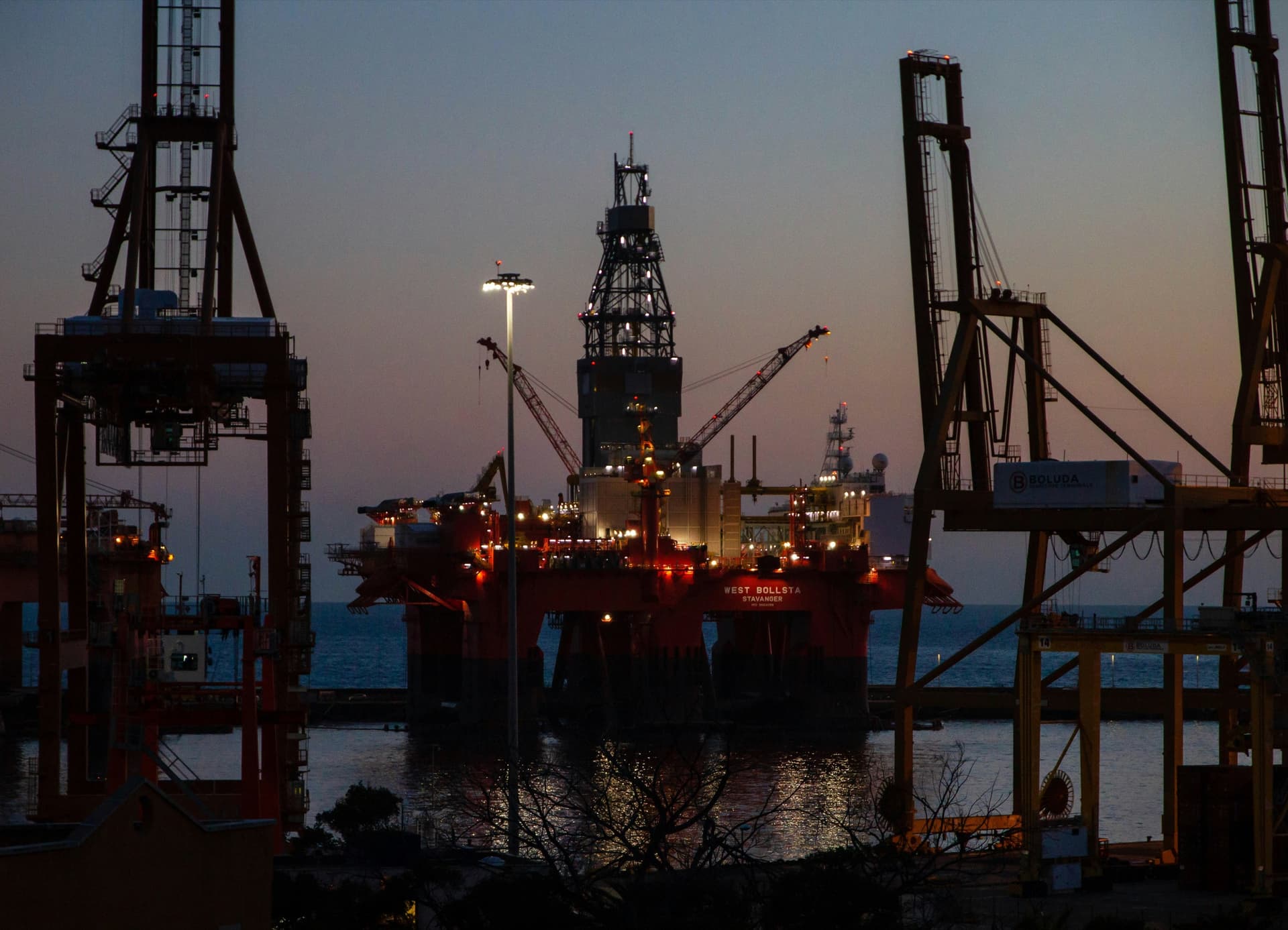 Offshore energy platform and port cranes at dusk for petroleum logistics